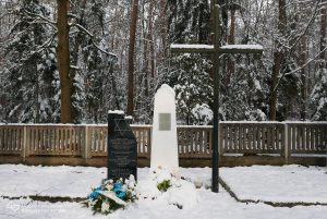 Zdjęcie współczesne. Zimowa sceneria. Widok na dwa pomniki i krzyż na cmentarzu Jagielle-Niechciałkach. Przed pomnikami złożone kwiaty. W tle las.