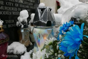 Zdjęcie współczesne. Zbliżenie na znicz i kwiaty przed pomnikiem na cmentarzu w Jagielle-Niechciałkach.