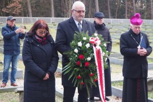 Dwóch przedstawicieli MPRŻ z wiązanką biało-czerwonych kwiatów. W tle cmentarz wojenny w Jagielle-Niechciałkach