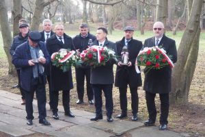 Delegacje z wiązankami biało-czerwonych kwiatów. W tle ogród Jarosławskiego Opactwa.