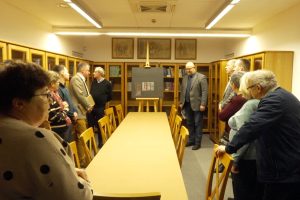 Prezentacja obrazu Kolbuszowa w Pracowni Naukowej Akademii Sprawiedliwych. Dookoła biblioteczki z książkami. Widzowie podziwiają dzieło.