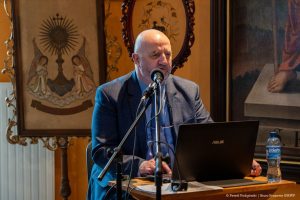 Artur Dobrucki siedzi przy biurku podczas prelekcji.