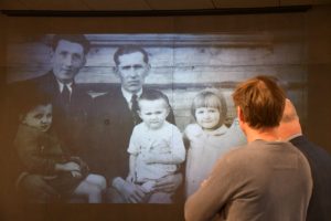 Zwiedzający oglądają prezentację zdjęć wyświetlaną na ścianie.