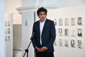 Prelegent przemawia. W tle obrazy więźniów KL Auschwitz.