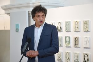 Prelegent przemawia. W tle obrazy więźniów KL Auschwitz.