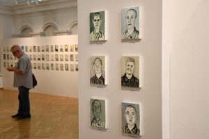 Fragment sali wystawowej. Na ścianach widzą małe portrety więźniów KL Auschwitz.