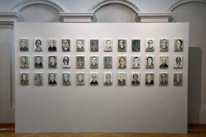 Fragment ekspozycji. Na ścianach widzą małe portrety więźniów KL Auschwitz.