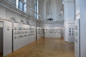 Fragment sali wystawowej. Na ścianach widzą małe portrety więźniów KL Auschwitz.