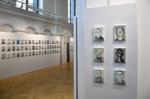 Fragment sali wystawowej. Na ścianach widzą małe portrety więźniów KL Auschwitz.