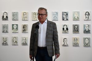 Prelegent przemawia. W tle obrazy więźniów KL Auschwitz.