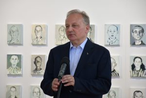 Prelegent przemawia. W tle obrazy więźniów KL Auschwitz.