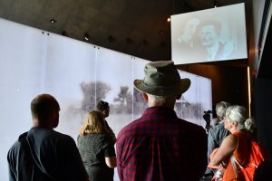 Grupa osób zwiedza ekspozycję muzealną z przewodnikiem.