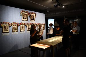 Grupa osób zwiedza ekspozycję muzealną z przewodnikiem.