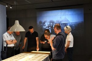 Grupa osób zwiedza ekspozycję muzealną z przewodnikiem.