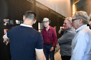 Grupa osób zwiedza ekspozycję muzealną z przewodnikiem.