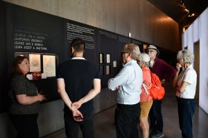 Grupa osób zwiedza ekspozycję muzealną z przewodnikiem.