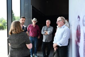 Grupa osób zwiedza ekspozycję muzealną z przewodnikiem.