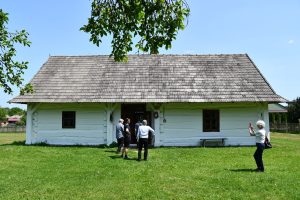 Grupa osób przed starą chałupą.