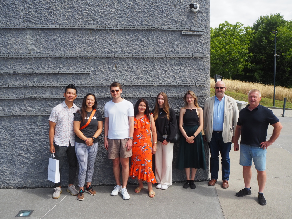 Grupa osób pozuje na tle Ściany Pamięci MPRŻ