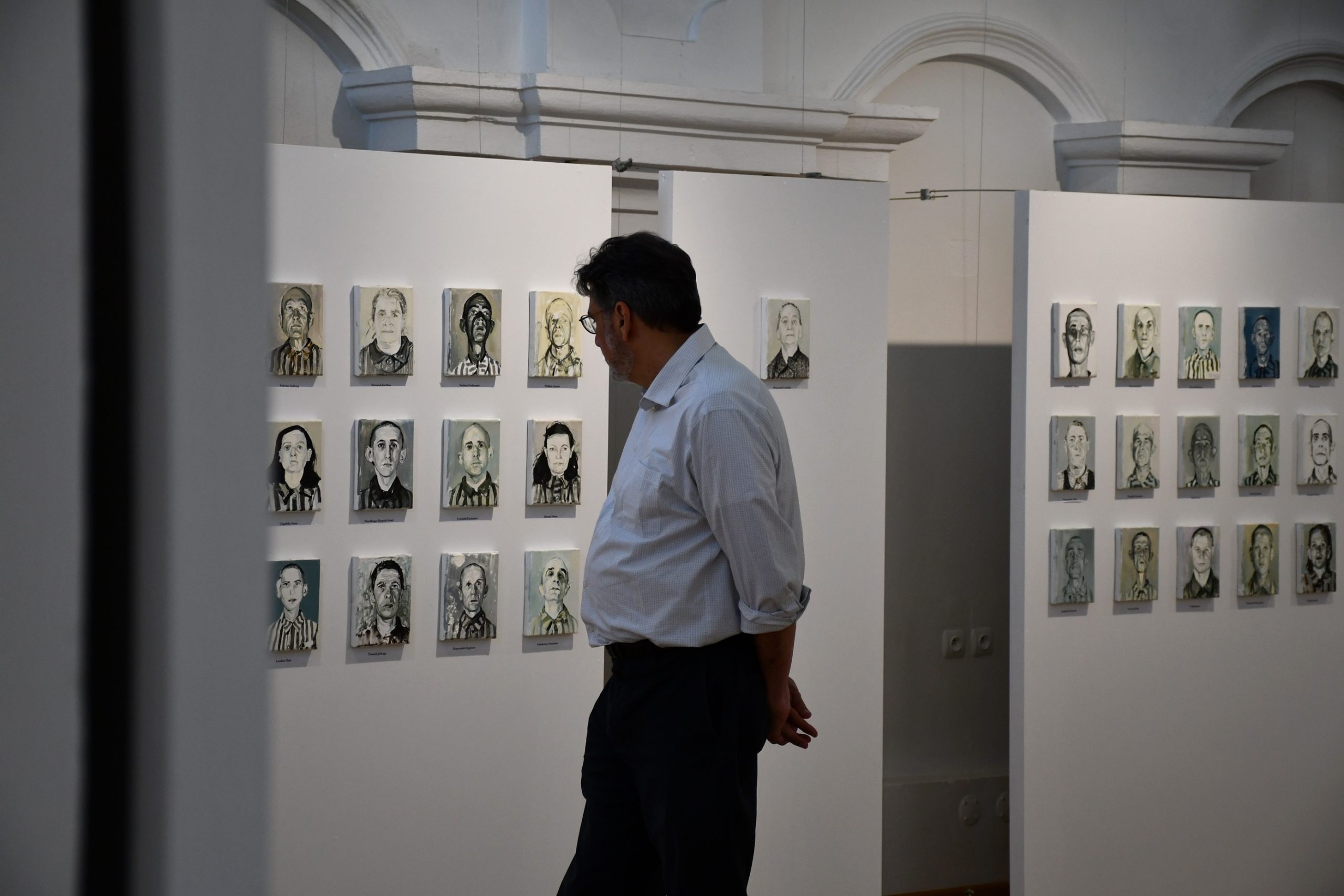 Mężczyzna zwiedza wystawę portretów olejnych.