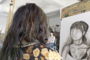 Uczennica szkoły plastycznej rysuje portret. W tle model.